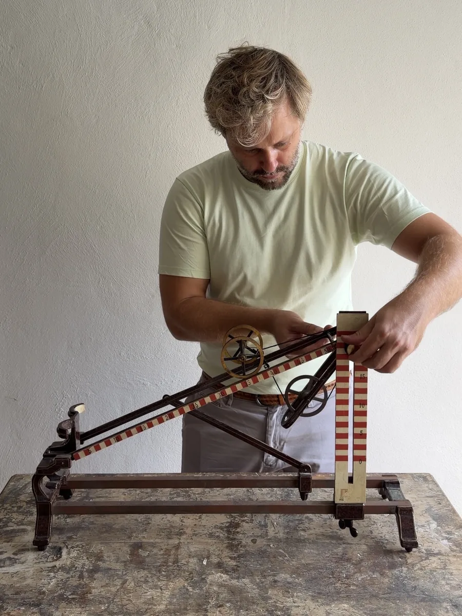 Florian Radinger stellt einen historischen physikalischen Demonstrationsapparat mit Rollen und Messskalen ein.