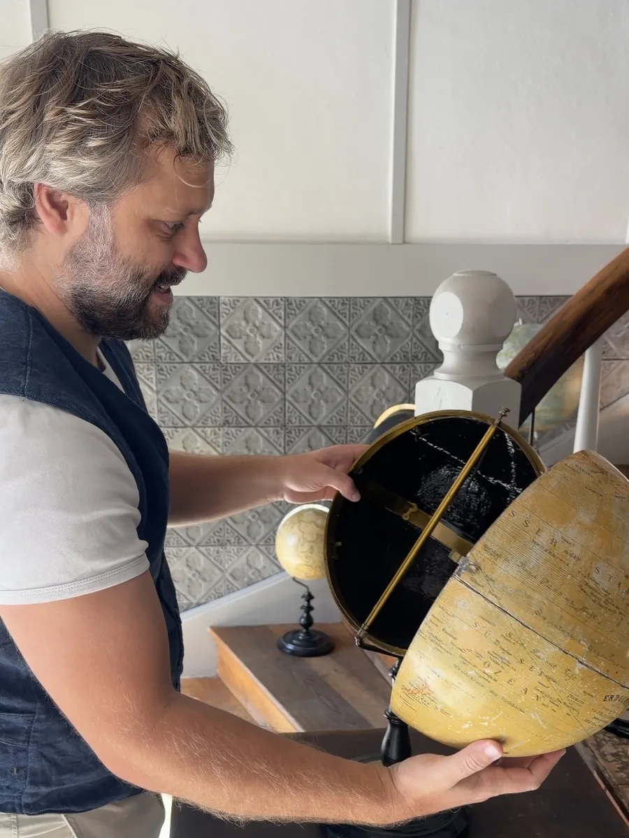 Florian Radinger öffnet einen historischen Globus, dessen Inneres schwarz ausgemalt ist.